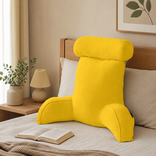 Yellow backrest reading pillow with arms on a bed in a cozy reading nook